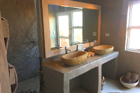 Bathroom in a Little Kulala Camp guest villa showing double vanity sinks in front of a large mirror, and access to the shower behind..