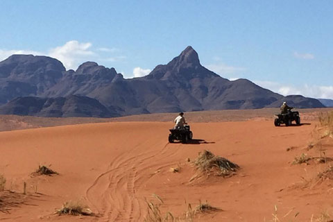 Deep tracks in the red sand of the Namib Desert lead to a quad bike situated in Sossusvlei Desert reserve. Some of the red petrified dunes tower behind forming a backdrop to this beautiful Namibian landscape.