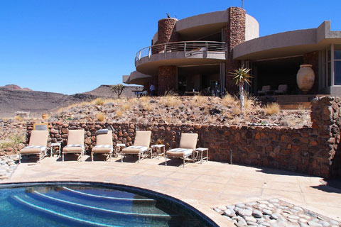 View from the Namib desert over a sparkling plunge pool with steps behind up to one of the guest villas at andBeyond Sossusvlei Desert Lodge in Namibia.